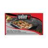 Die Verpackung einer keramischen Grillplatte von Weber. Auf der Verpackung ist die Grillplatte abgebildet, die mit gegrilltem Gemüse und Garnelen belegt ist. Die Grillplatte selbst hat einen rechteckigen, flachen Körper und wird auf einem Grillrost verwendet. Der Hintergrund zeigt verschiedene Zutaten und eine Grillumgebung. Das Weber-Logo befindet sich oben auf der Verpackung. Die Verpackung enthält Text in mehreren Sprachen, darunter auch „Keramik-Grillplatte“ in Deutsch.