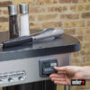 Nahaufnahme eines Weber Performer Premium GBS Holzkohlegrills mit Gewürzmühlen, einer Grillzange und einer Hand, die einen digitalen Timer bedient.