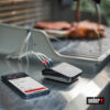 Weber Connect Smart Grilling Hub neben einem Smartphone mit der Weber Connect App und zwei Fleischstücken auf einem Grill.