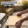 Zwei Hände legen ein rechteckiges, hellbraunes Weber Works Schneidebrett mit einer umlaufenden Saftrille auf einen Grill. Der Text "cooles Design & SAFTRILLE" ist über dem Schneidebrett eingeblendet.
