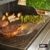 Weber Precision Grillwender unter einem gegrillten Steak auf einem Grillrost mit weiteren Steaks, Kartoffelecken und Spargel.