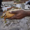 Eine Hand hält ein belegtes Sandwich, das mit einer silbernen Grillspachtel von einem Grill genommen wird, mit dem Text "problemlos ZUBEREITEN" überlagert.