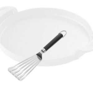Ein silberfarbener Weber Flexible Grillwender aus Edelstahl mit einem schwarzen, rutschfesten Griff. Im Hintergrund ist der verschwommene Umriss einer hellen, runden Grillplatte mit zwei Griffen zu sehen.
