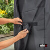 Hände befestigen einen schwarzen Weber Grill Cover mit einem Klettverschluss.