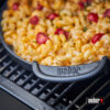 Nahaufnahme einer schwarzen Weber Gusseisenpfanne mit Mac and Cheese und Tomaten auf einem Grillrost.