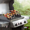 Ein silberner Weber Spirit E-330 Gasgrill mit Weber Gourmet BBQ System Sear Grate und einem Weber 7615 Etagensystem mit Spießen, auf denen Fleisch und Gemüse zubereitet werden.
