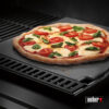 Pizza mit Tomaten, Mozzarella und Basilikum auf einem Weber Crafted Pizzastein auf einem Grillrost.
