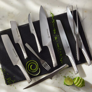 Silbernes Weber Deluxe Messer-Set mit verschiedenen Messertypen, einer Gabel und einer Grillzange auf einer schwarzen Schieferplatte, garniert mit Limettenspiralen und -scheiben.